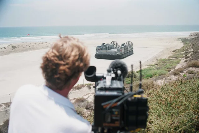 A videographer shoots a scene as a Landing Craft Air Cushion (LCAC) prepares to cross the surf during filming for a History Channel special to air in August. The series entitled, "Mail Call with Lee Ermey" will focus on explaining the vast complexities of military technology and the uniformed people. Copyright and music licensing for US videography client work, explained