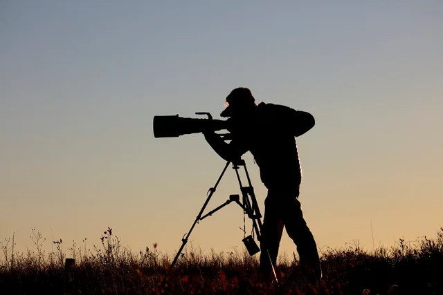 NPS | N. Lewis Brett Raeburn, Park Visual Information Specialist, captures video of bucks in rut at Big Meadows during sunset. Camera, Tripod, Big Lens (SNP0096_VideographerSilhouette_nl). What to Include in Videography Services Packages