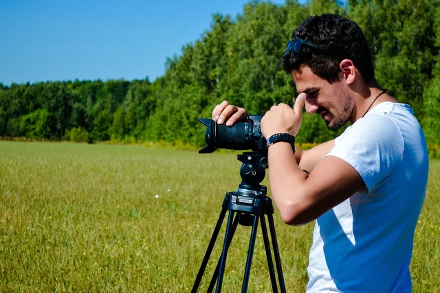 man, camera, photographer, videographer, equipment, tripod, field, grass, photoshoot, nature, cinema. Videography pricing models and the risk each one hides